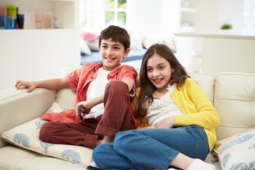 Two Hispanic Children Sitting On Sofa Watching TV Together