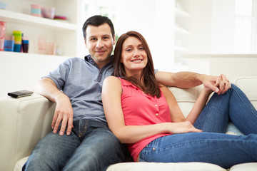 Hispanic Couple Sitting On Sofa Watching TV Together