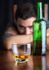 Glass of whisky with an out of focus drunk and depressed man