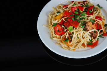 Noodles with vegetables on plate isolated on black