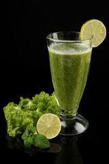 Glass of green vegetable juice and lime isolated on black