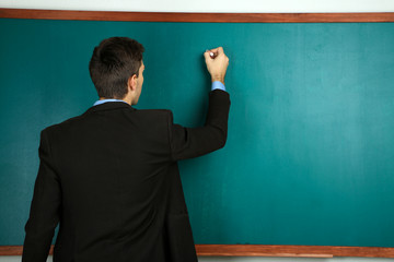 Young teacher near chalkboard in school classroom
