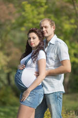 Young man with his pregnant wife posing on open air