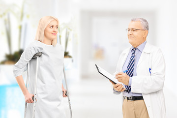 Male doctor talking to female patient with crutches in hospital