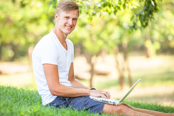 Teen boy with laptop in the park.