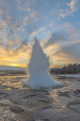 Eruption of Strokkur Geyser against setting sun in Iceland