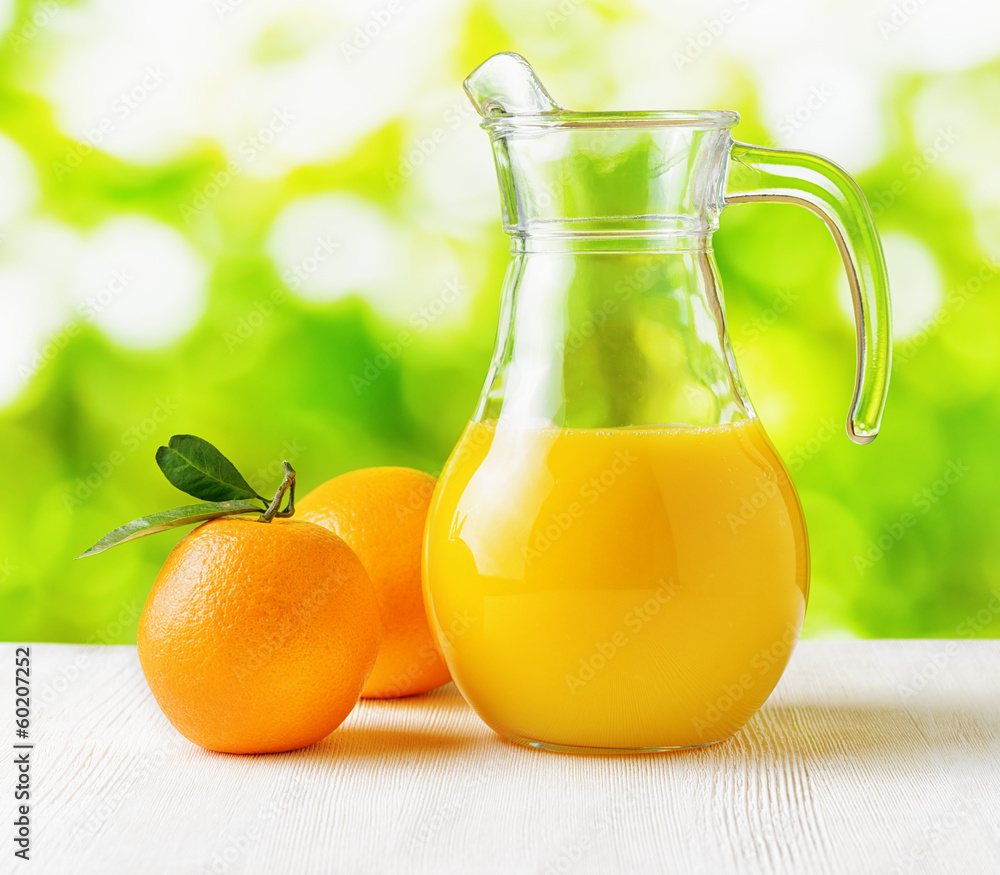 Wall mural Jug of orange juice on nature background