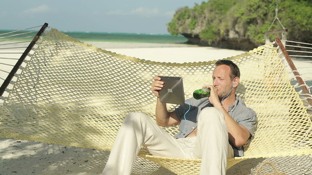 Young man watching funny movie on tablet while sitting on hammoc