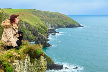 Woman sitting on rock cliff looking to ocean Co. Cork Ireland