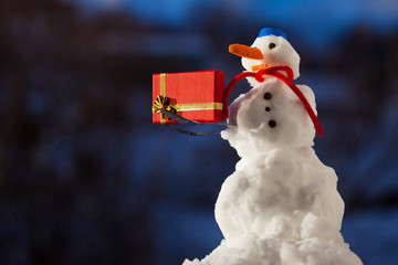 Little happy snowman with gift box outdoor. Winter season.