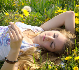 Young blond woman enjoys the spring between dandelions