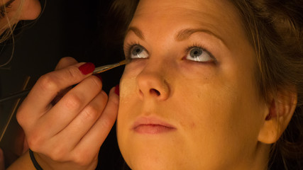 Woman applying make up for a bride in her wedding day near mirro