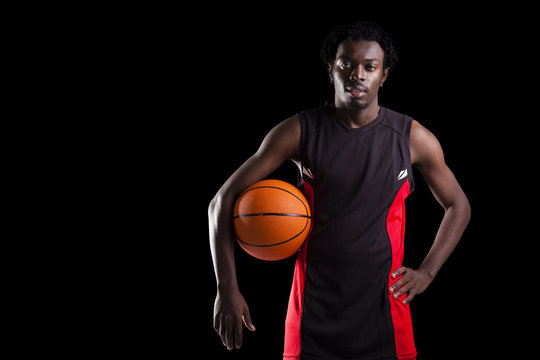 Portrait of a basketball player holding a ball against dark back
