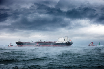 A tanker and tugboats on sea during a violent blizzard.