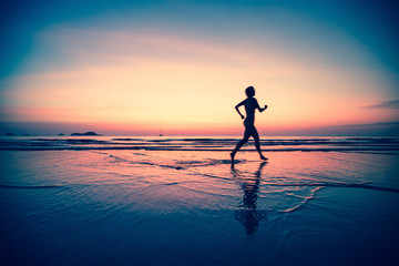 Silhouette of a woman jogger on the beach at sunset.