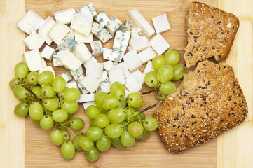 Wooden board with grape, cheese and bread