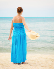 Fototapeta na wymiar Woman in blue dress throws hat on the beach