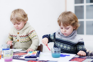 Two little twins boys having fun indoor, painting with different