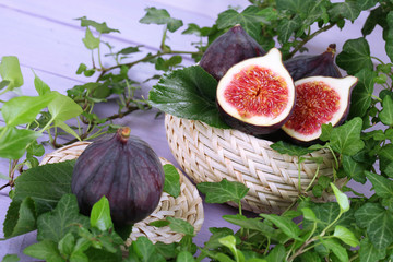 Ripe figs in basket in leaves on wooden table close-up