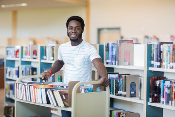 Librarian With Trolley Of Books In Library