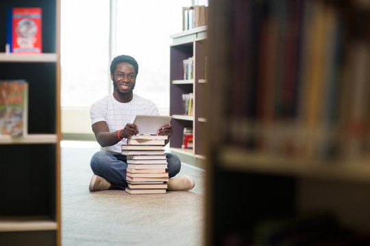 Student With Books And Digital Tablet Sitting In Library