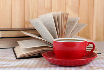Cup of coffee and books on tablecloth on wooden background