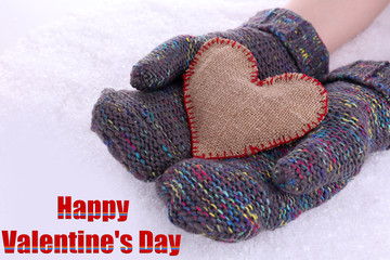 Female hands in mittens with heart on snow background