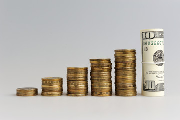 Пять стопок монет и сверток долларов на сером фоне