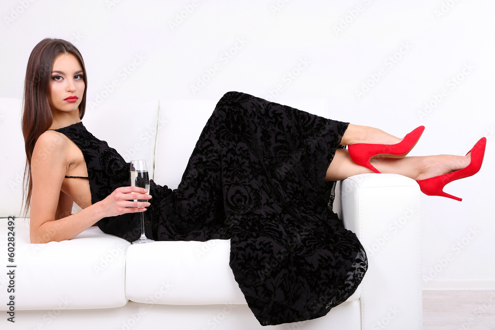 Poster Beautiful young woman in black dress on sofa on white