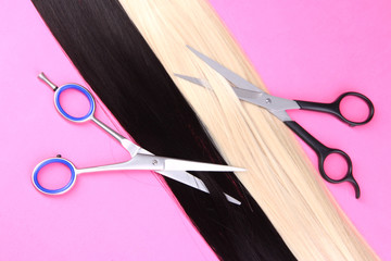 Long black and blond hair with scissors on pink background