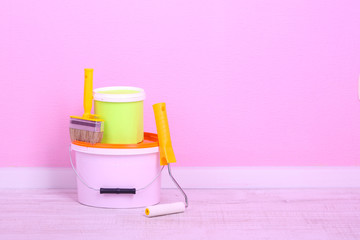 Paints, roll and paintbrush on floor in room on wall background