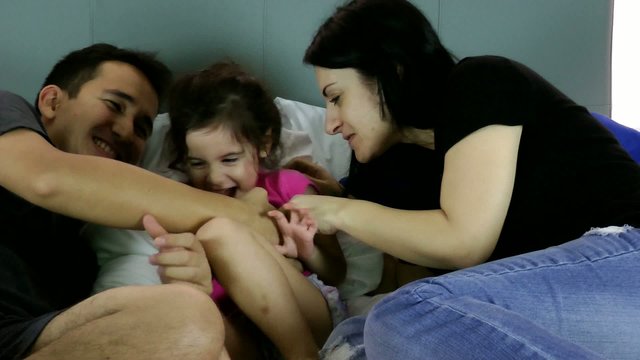 Parents tickling their child on bed at home