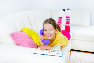 Cute little girl is reading book and telephone