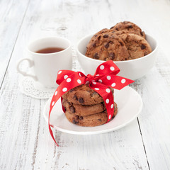 Chocolate chip cookies on a white plate with cup of tea