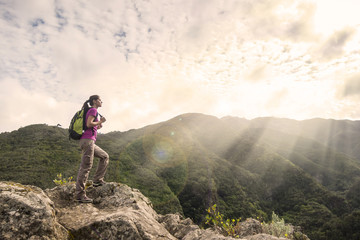 woman hiker with backpack standing on top of a mountain and enjo