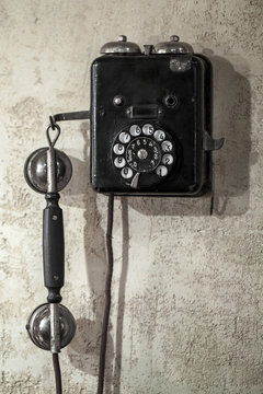 Vintage black phone hanging on old gray concrete wall