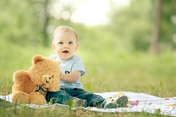 little boy playing with a teddy bear in the grass