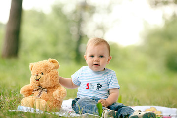 little boy playing with a teddy bear in the grass