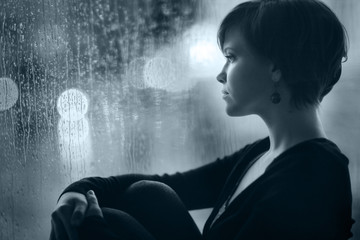 Naklejka premium sad girl on the windowsill looking out the window