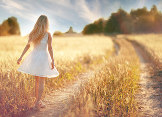 Fototapeta na wymiar happy girl on the road in a wheat field at sunset