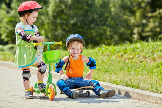 Little boy sits on skateboard,little girl stay near