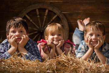 Three laughing children on hay in a hangar © Alexandr Vasilyev