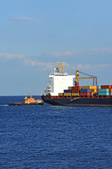 Tugboat assisting container cargo ship to harbor quayside
