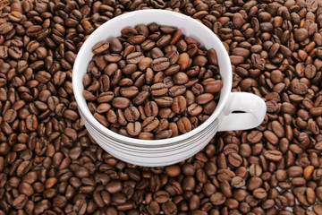A cup full of coffee beans surrounded by more coffee beans