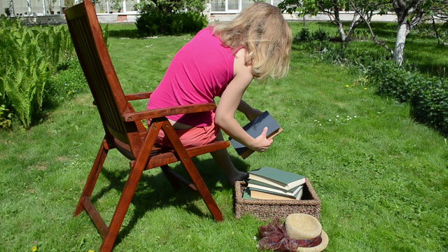 Woman sit on wooden chair and read old books in garden