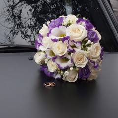 Beautiful bouquet and wedding rings on black car