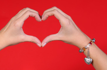 Fototapeta premium Female hands making a heart shape over red background