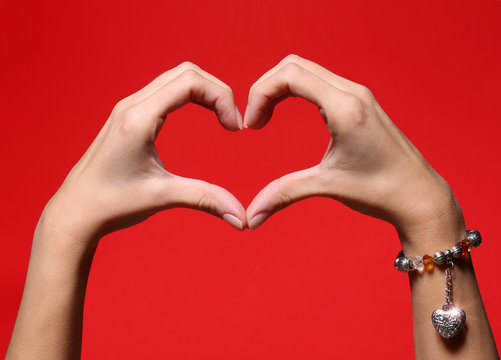 Female hands making a heart shape over red background