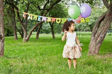 Little girl stands in park, holding three air balloons
