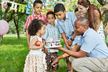 Little girl with big apple blows out candle on birthday cake